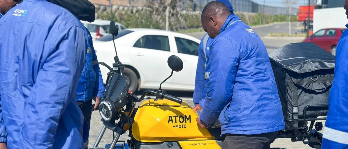 Fleet operators inspecting an Atom-Moto yellow electric delivery motorcycle